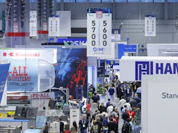 Recinto de una feria industrial abarrotado, con numerosos stands de empresas que exhiben carteles con los colores azul y rojo de sus marcas, así como pantallas digitales.